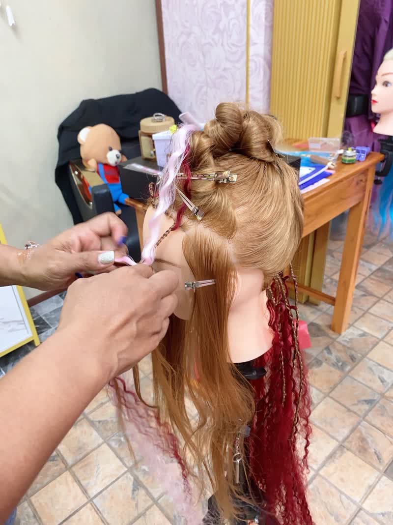 Pink and red extensions being braided into blonde hair